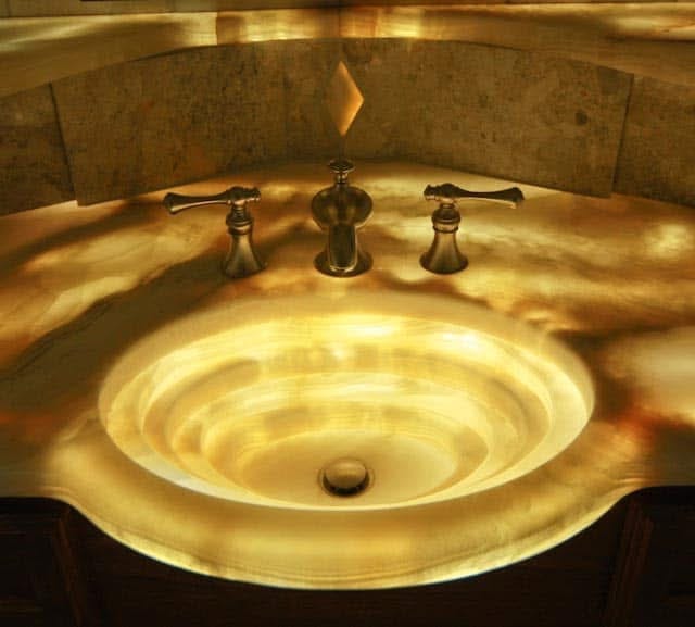 Close-up of onyx shower niche detail with backlit amber ceiling and polished stone surfaces
